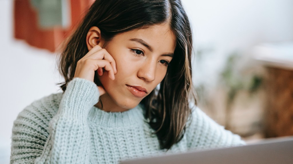 Young adult at a laptop, looking pensively